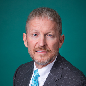 Male pediatrics provider smiling in front of a teal blue backdrop.