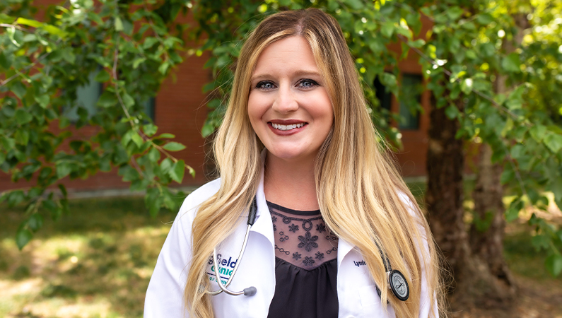 Female with long straight hair wearing white medical coat smiling in outdoor setting