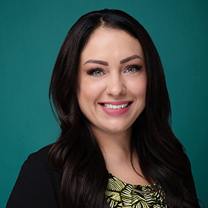 Female nurse practitioner with long dark hair smiling in front of green photo backdrop.