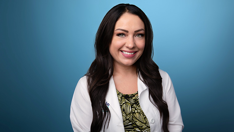 Female nurse practitioner wearing white medical coat smiling in professional headshot.