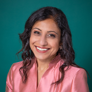 Female doctor smiling in front of a teal blue backdrop.