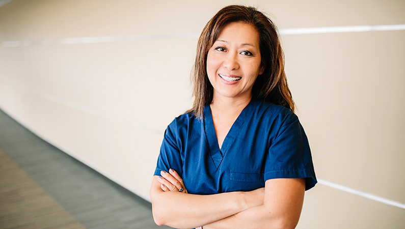 Female wearing navy scrubs with dark hair smiling while posing in a hallway