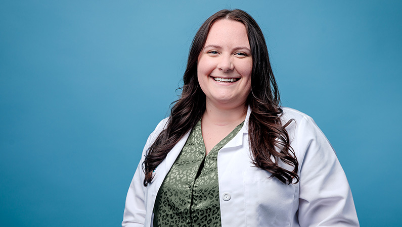 Dark haired female medical professional smiling in front of light blue backdrop