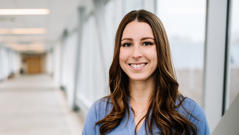 Female chiropractic provider smiling in a naturally lit  hallway.
