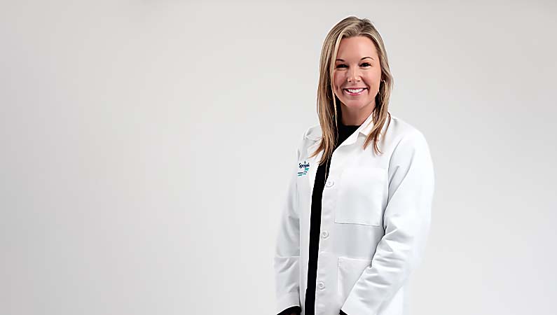 Female certified nurse midwife smiling in front of a white photo backdrop.