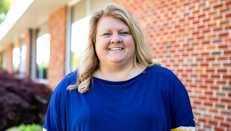 Female with light hair wearing blue top smiling outside of a brick office building