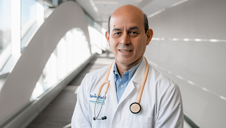 Male cardiologist wearing white medical coat smiling.