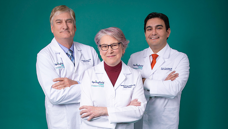Group of medical professionals smiling with their hands crossed in front of a green background