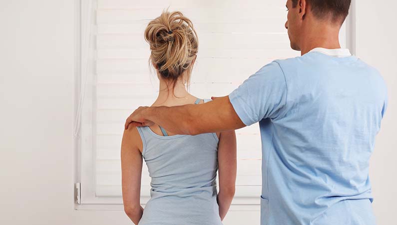 Patient sitting on a chiropractic table having back checked by chiropractor.