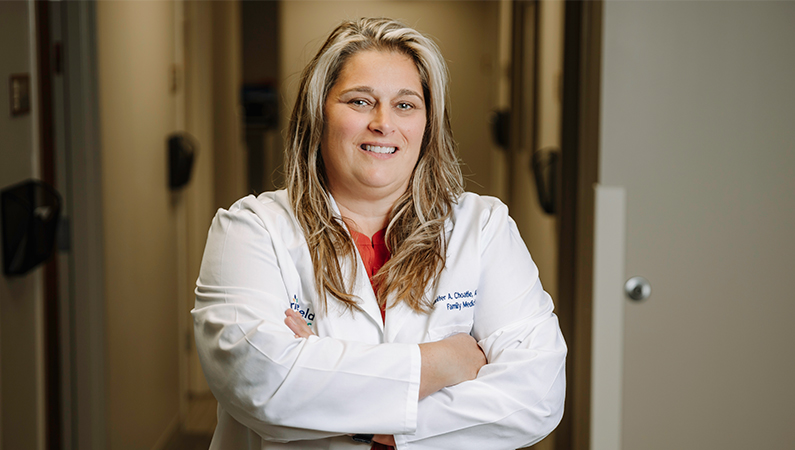 Female nurse practitioner in white coat posing in a doctor's office hallway.