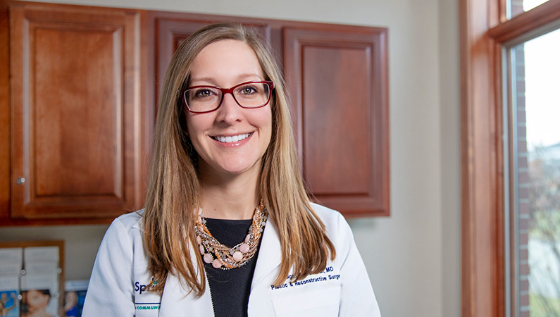 Woman wearing a white doctors coat smiling in a well lit patient room.