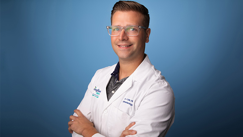 Male physician assistant smiling in front of blue photo backdrop.