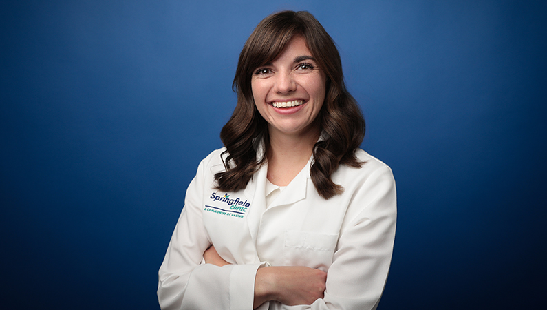 Female family medicine physician smiling in front of blue photo backdrop.