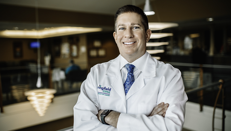 Male doctor wearing a white coat smiling with arms crossed.