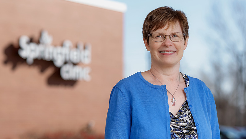 Female internal medicine doctor smiling in outdoor setting.