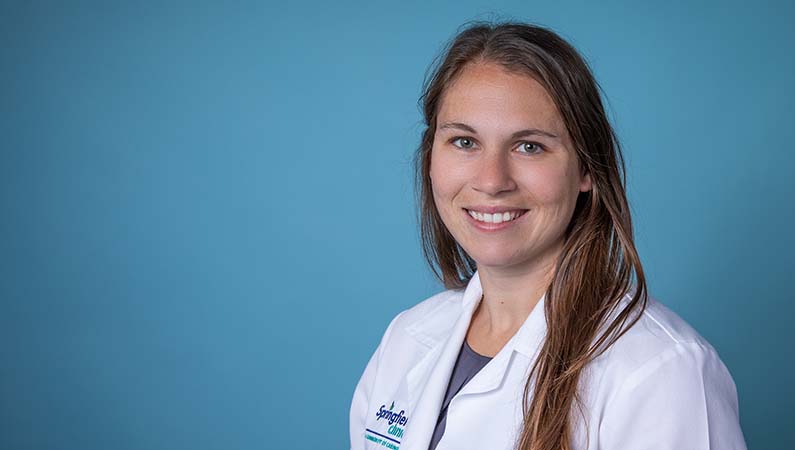 Female physician assistant smiling in front of a blue backdrop.
