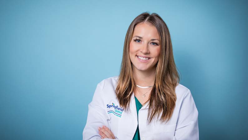 Female critical care nurse practitioner in white coat smiling.