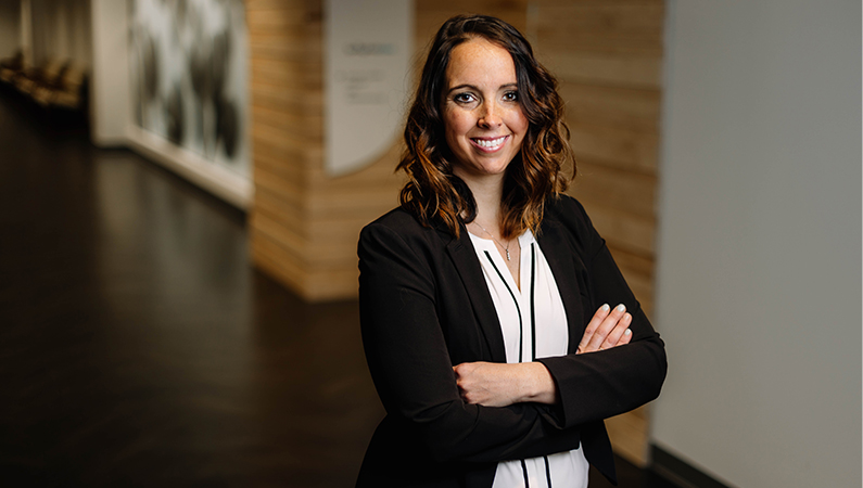 Female nurse practitioner smiling with arms crossed in a dim hallway.