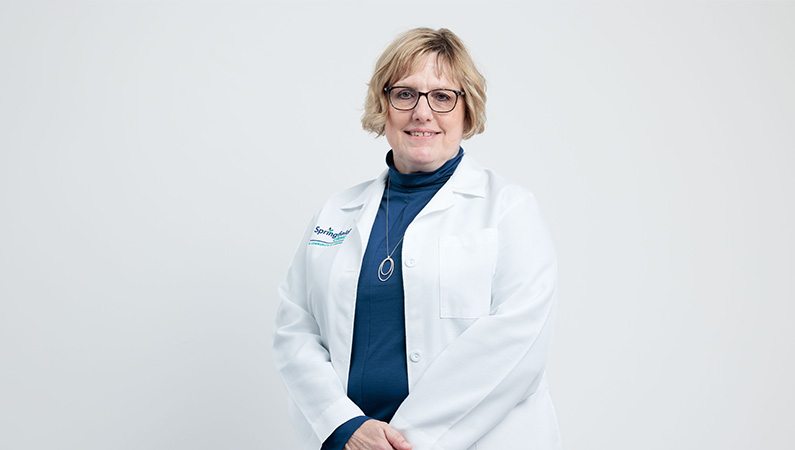 Female certified nurse midwife smiling in front of a white photo backdrop.