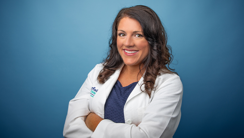 Female nurse practitioner in white lab coat smiling in front of a light blue photo backdrop.