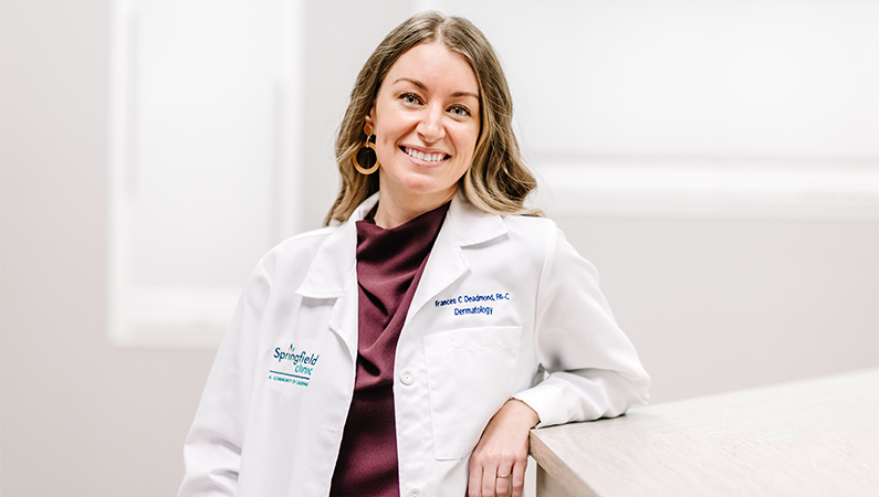 Female physician assistant in a white coat smiling in a bright office setting.