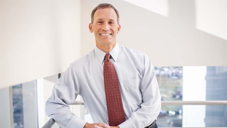 Male orthopedics doctor in dress shirt and tie smiling at camera on a staircase in a naturally lit building.