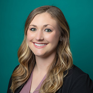 Female nurse practitioner professional headshot in front of a teal blue backdrop.