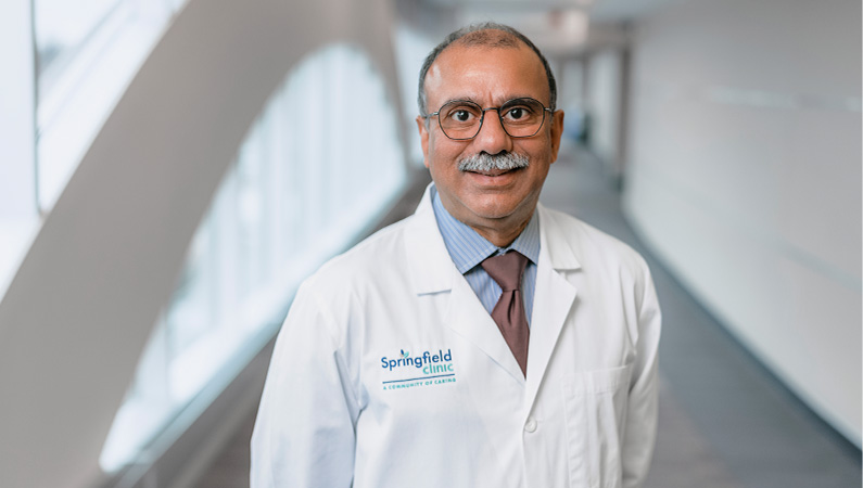 Male cardiologist wearing white medical coat smiling.