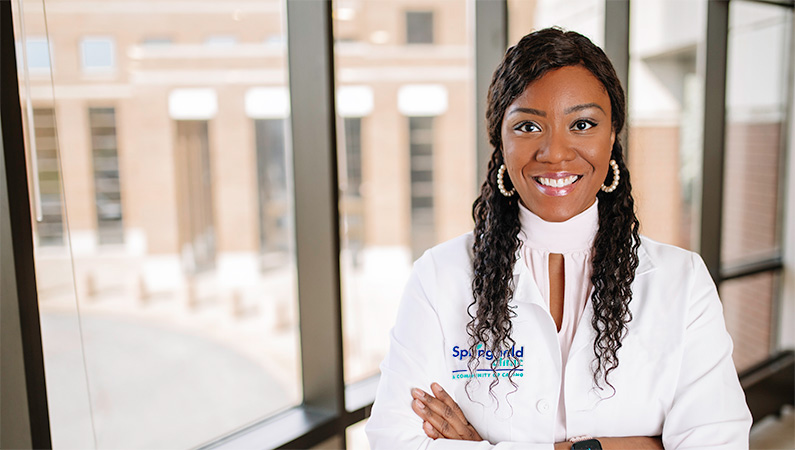 Woman wearing white doctors coat in front of a window.