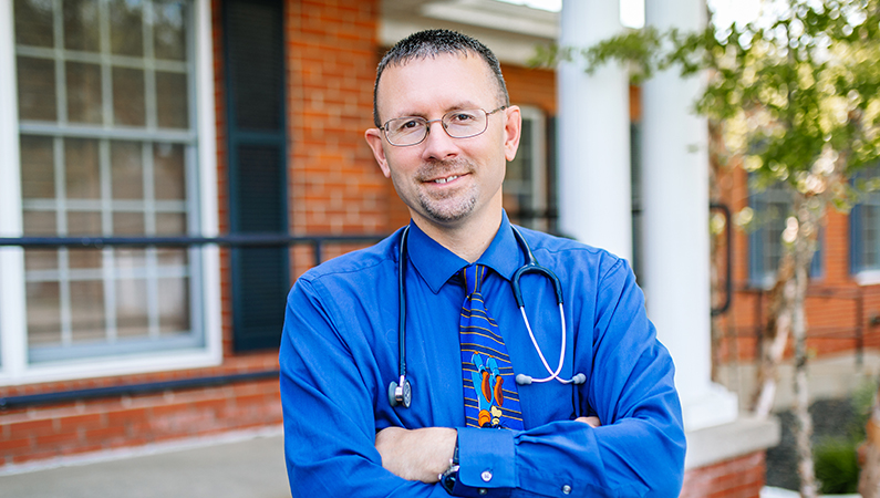 Man smiling with his arms crossed outside in front of the brick doctors office.