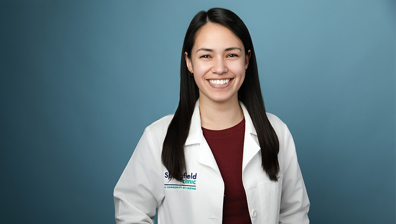 Female wearing white medical coat smiling in front of light blue backdrop