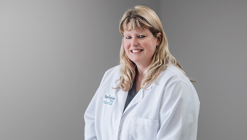 Female podiatrist wearing white medical coat smiling in medical office setting.