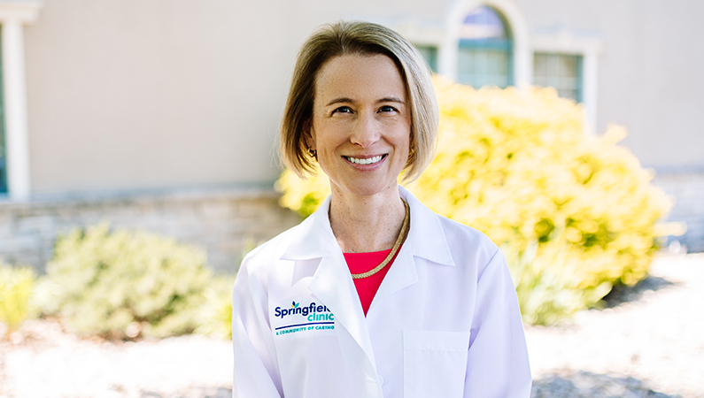 Dr. Penelope Ewbank, allergist in Peoria, smiling in front of Springfield Clinic Peoria Allergy and Asthma on a bright day.
