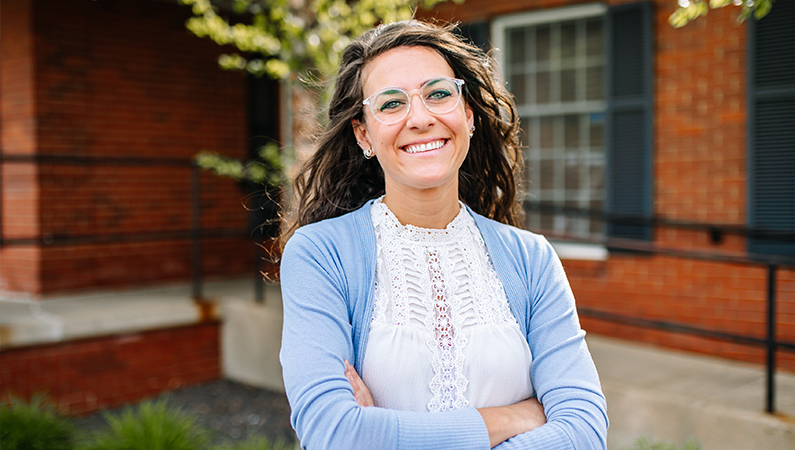 Woman smiling with her arms crossed outside in front of the brick doctors office.