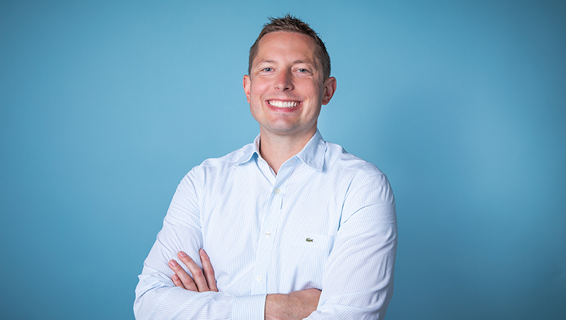 Male smiling against a light blue backdrop.
