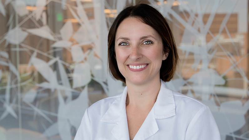 Woman wearing white doctors coat smiling in a well lit hallway