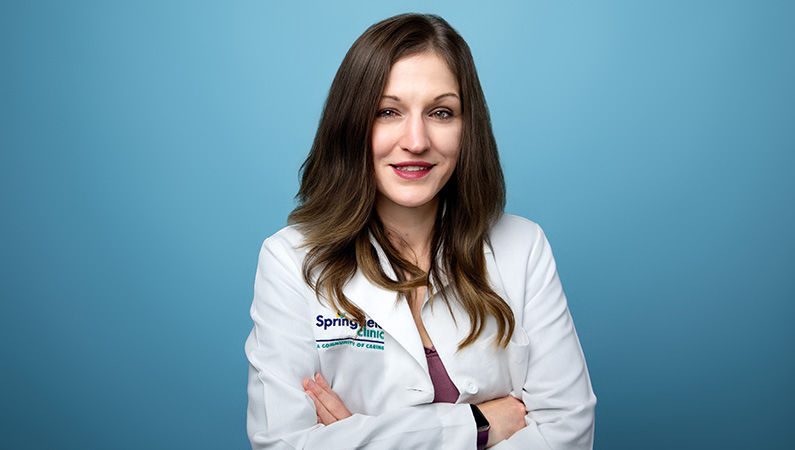 Female wearing white medical coat smiling in front of blue studio background
