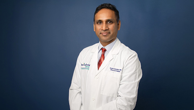 Male critical care medicine physician smiling in front of blue backdrop