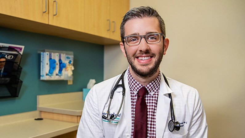 Man wearing a stethoscope around his neck, smiling in an exam room.