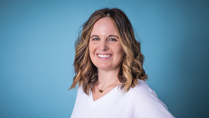 Woman smiling in front of a blue backdrop.
