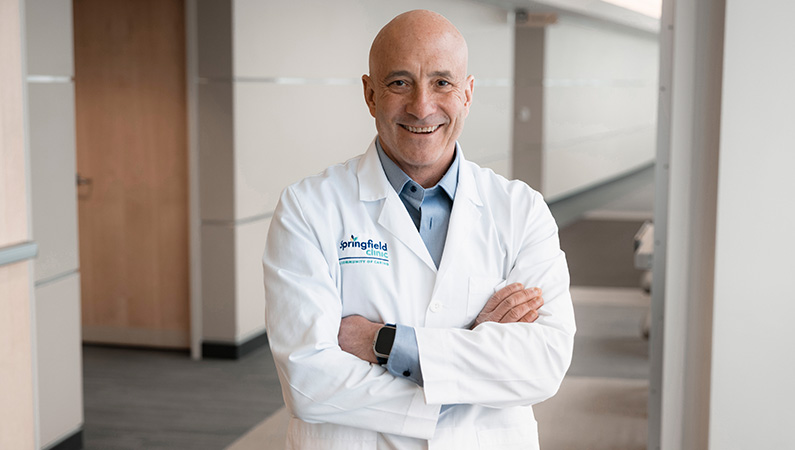 Male cardiologist wearing white medical coat smiling.