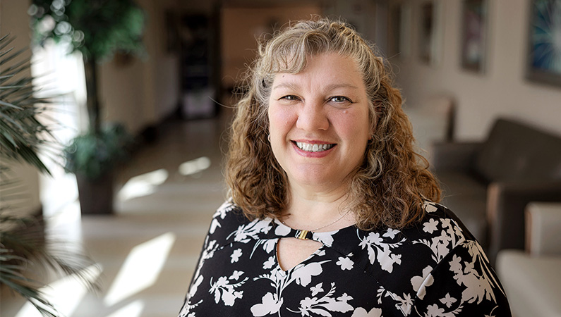 Female doctor in white lab coat smiling in medical facility hallway.