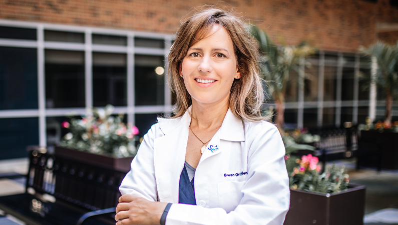 Female with short dark hair wearing white medical coat smiling in lobby setting