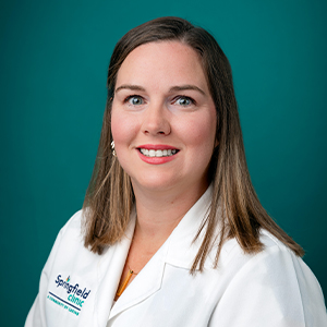 Female nurse practitioner in white coat smiling in a professional headshot.