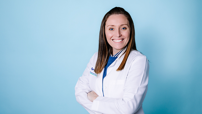 Female nurse practitioner smiling in front of a blue background.