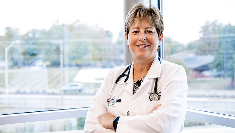 Woman wearing stethoscope around her neck, smiling in front of a window.