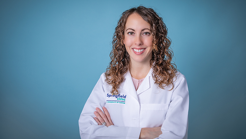 Female nurse practitioner wearing white coat smiling with a blue backdrop.