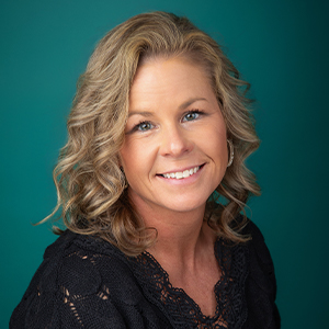 Female nurse practitioner smiling in front of green photo backdrop.