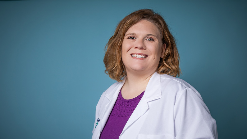 Female nurse practitioner smiling in front of a blue backdrop.