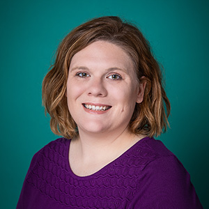 Female nurse practitioner professional headshot in front of a teal blue backdrop.